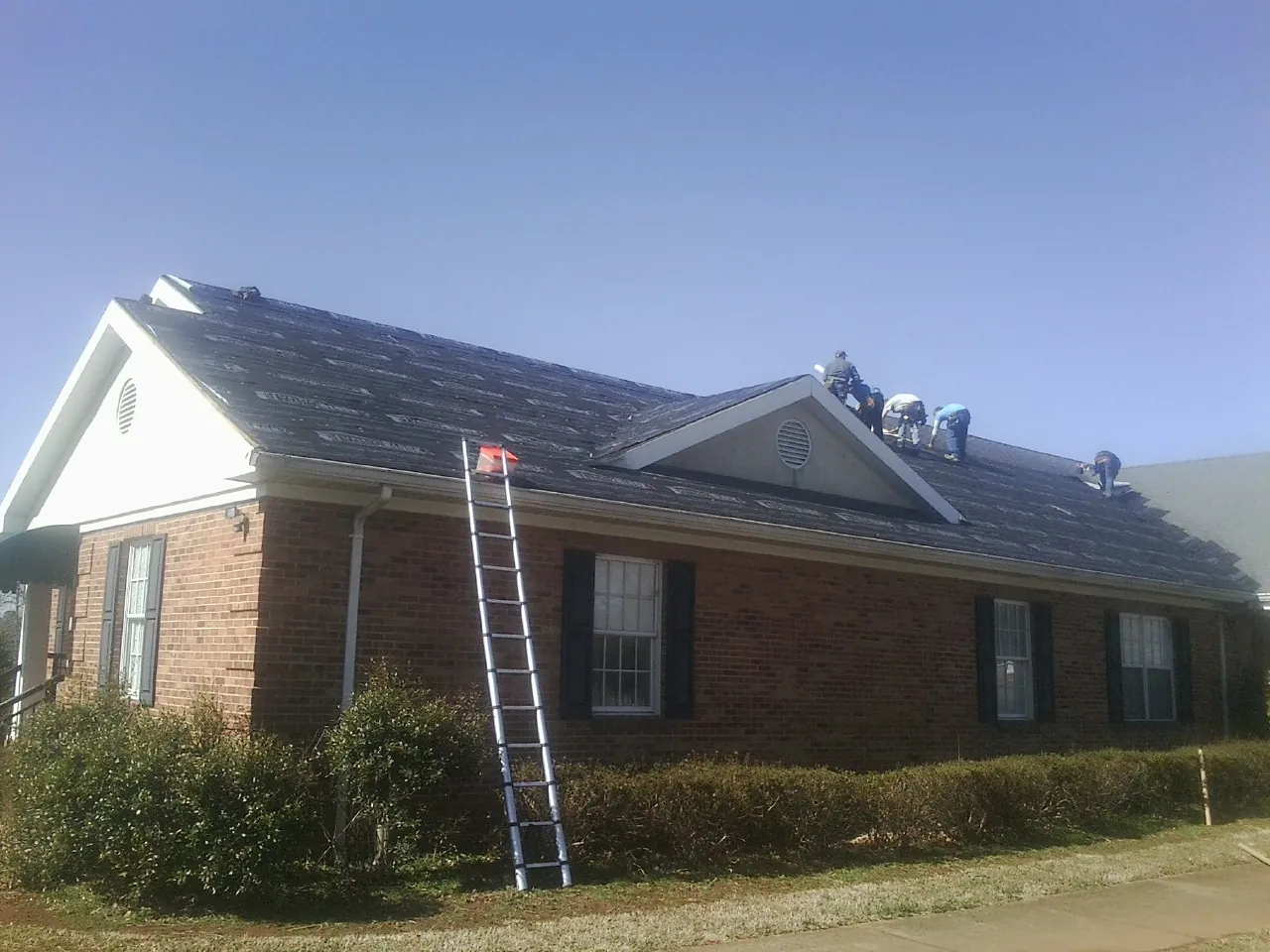 Crew tearing shingles off a brick ranch roof with a ladder set — Emergency Roof Repair work by our crew in Latrobe