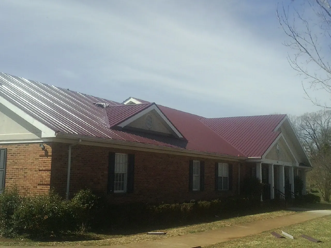 Red metal roof with gabled entries on a long brick building, from a Hail Damage Roof Repair job in Latrobe