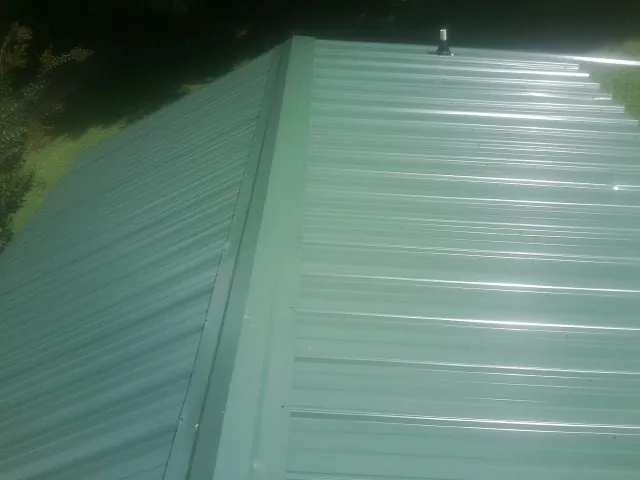 New green metal panels meeting at the ridge of a roof — Flat Roof Repair work by our crew in Latrobe