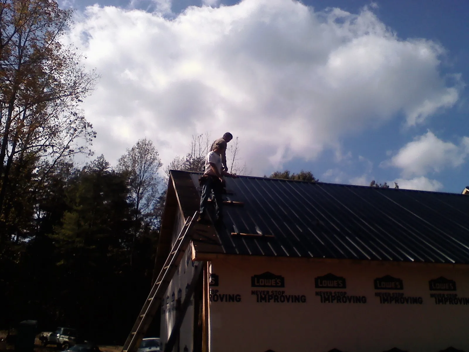 Roofer fastening dark metal panels high against a cloudy sky, from a Roof Inspection job in Latrobe