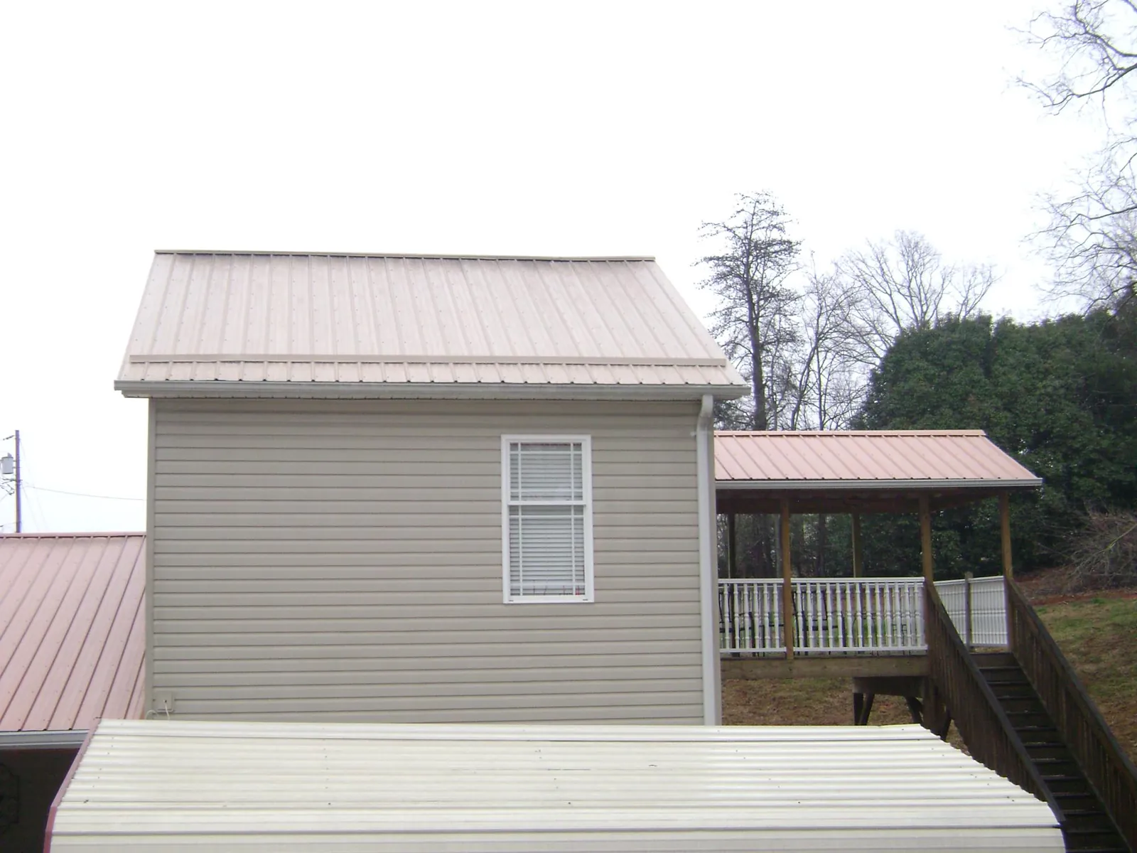 Tan metal roofs on a two story addition and attached porch, from a Roof Replacement job in Latrobe